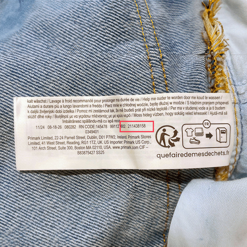 Une étiquette de composition et d'entretien et des symboles de certification cousus dans la couture d’un tissu en denim bleu, avec la référence du produit mise en avant par un encadré rouge.